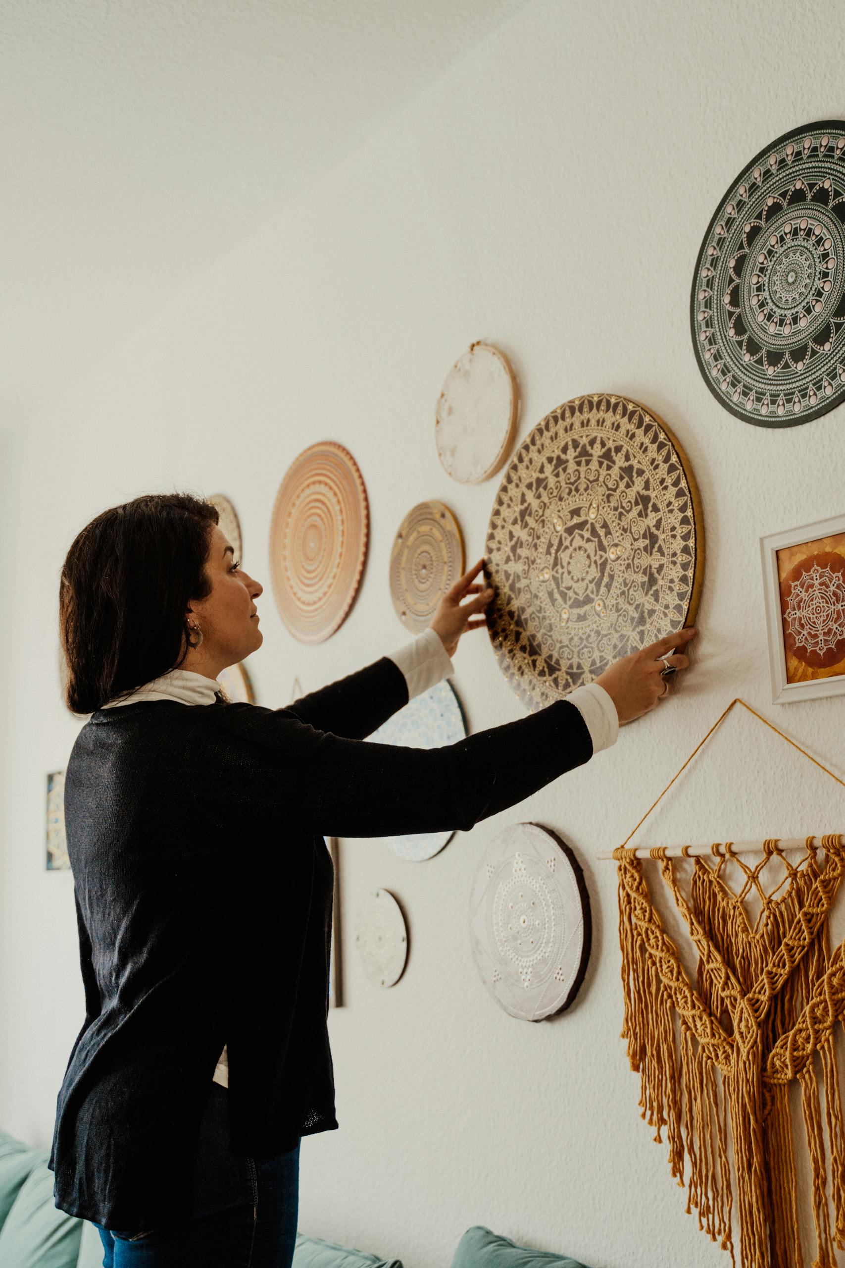 Adult woman decorates a well-designed interior wall with mandala art pieces.