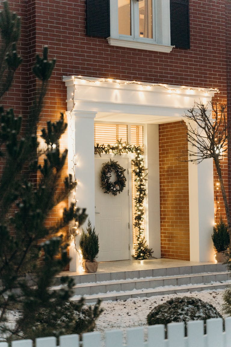 Charming brick house entrance decorated with Christmas wreath and lights in winter.