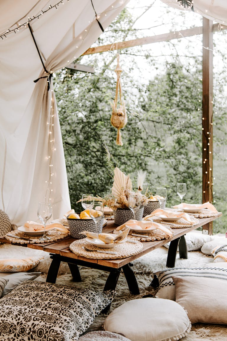 Elegant boho dining setup in outdoor garden with cozy pillows and table decor.