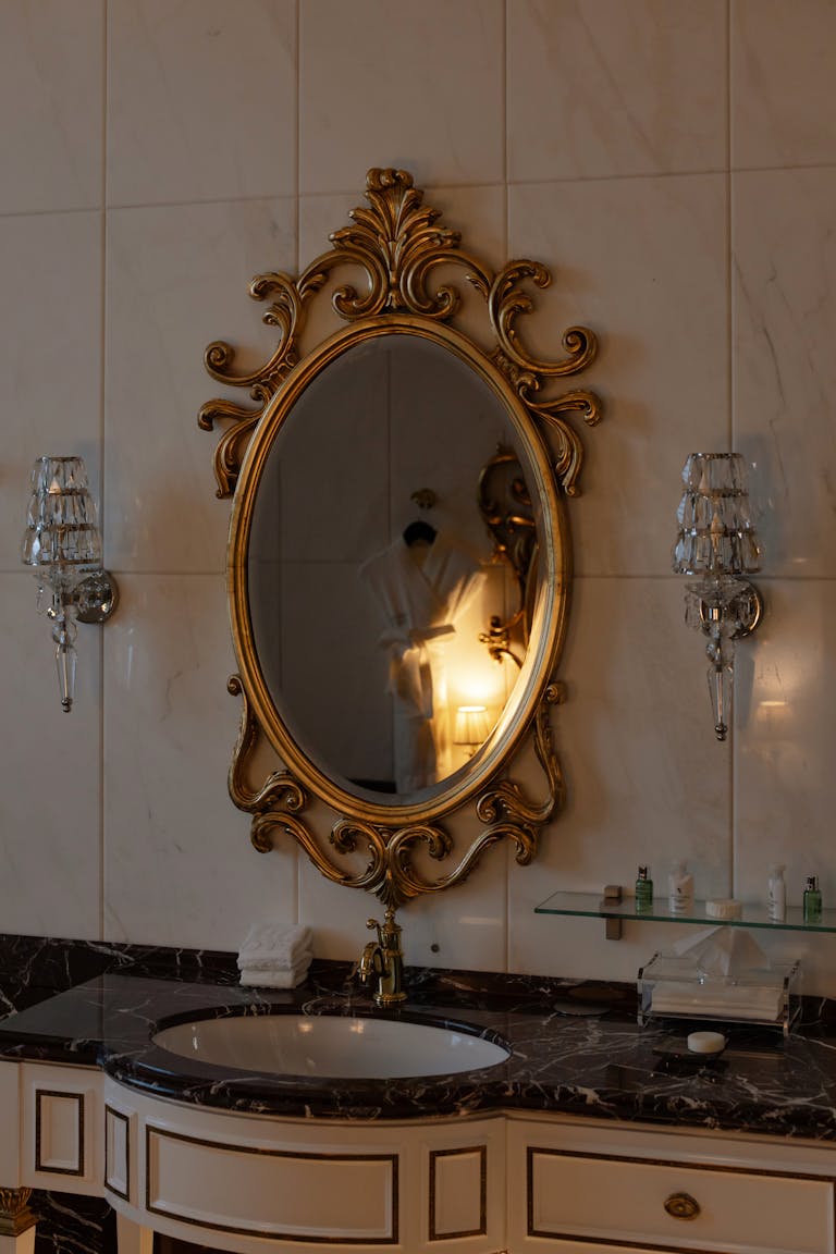 Luxurious bathroom with ornate oval mirror and classic lighting fixtures.