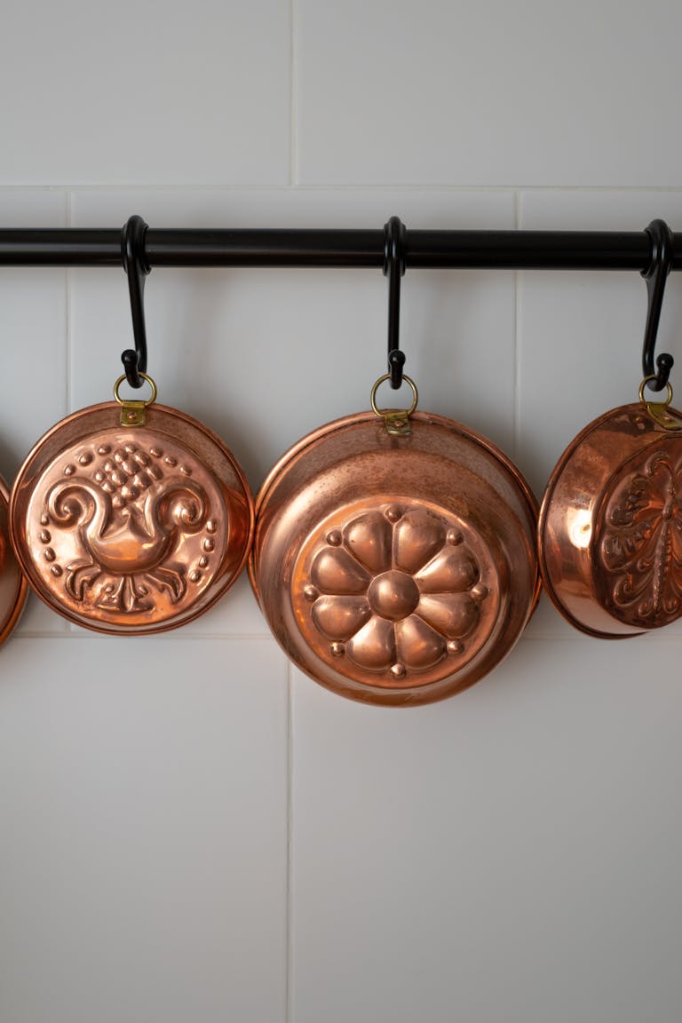 Old-fashioned copper baking molds hanging on black hooks in a vintage kitchen setting.