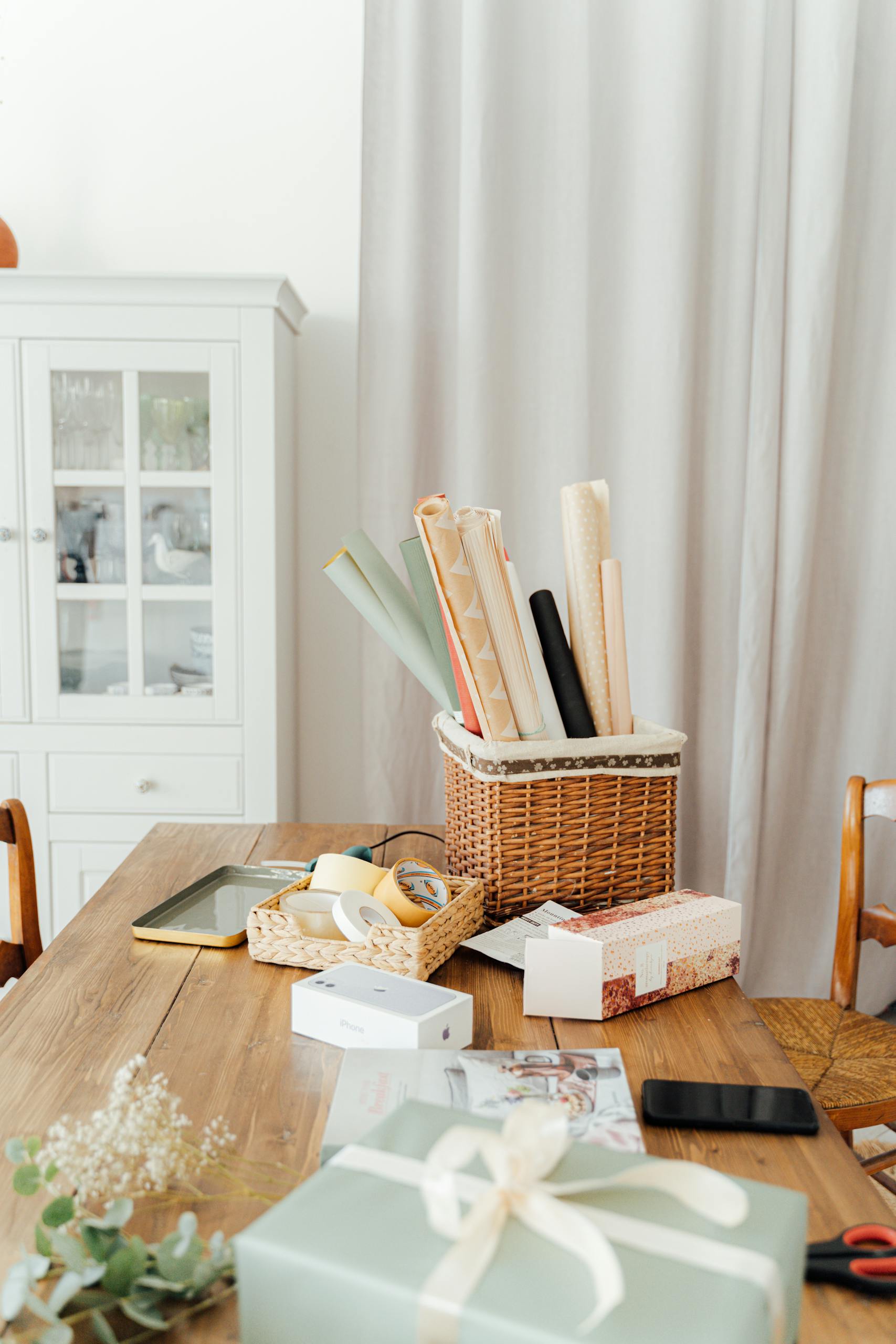 Stylish gift wrapping scene with ribbons and baskets on a wooden table indoors.