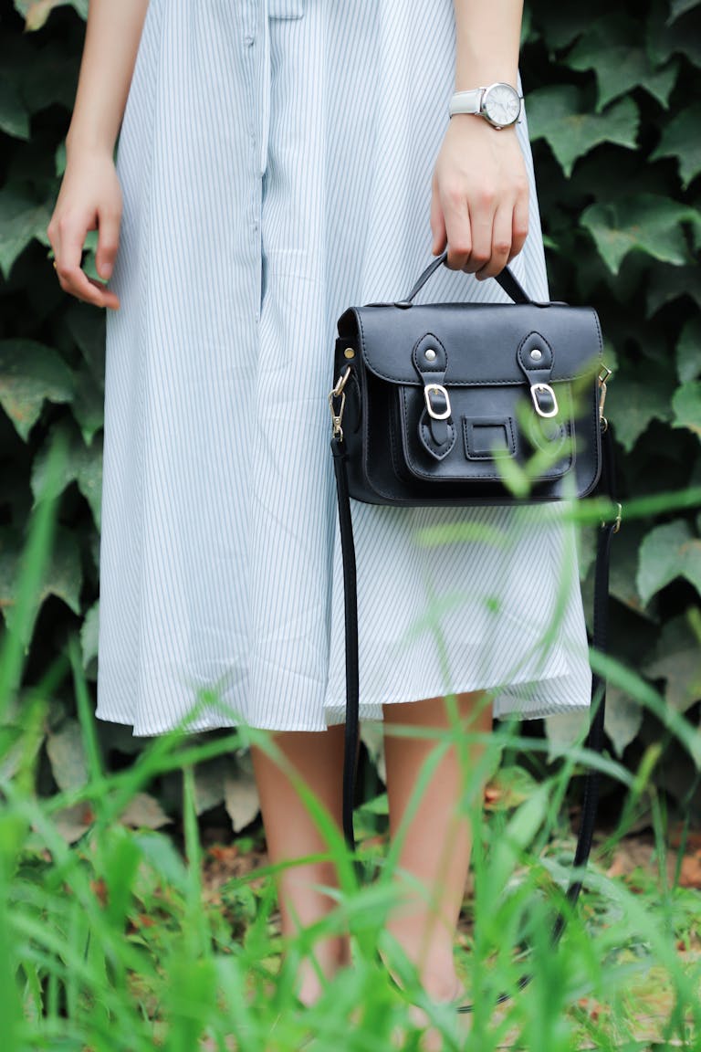 Stylish woman in striped dress holding a black handbag in a natural setting.