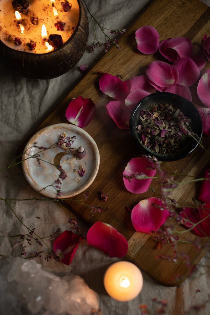 Top view of a rustic aromatherapy setup with candles and rose petals on a wooden board.