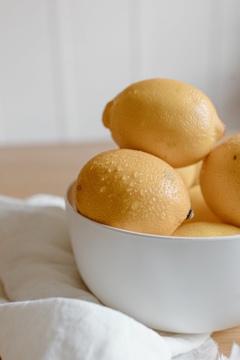 A bowl of fresh lemons on a wooden table with a light setting, perfect for healthy and organic themes.