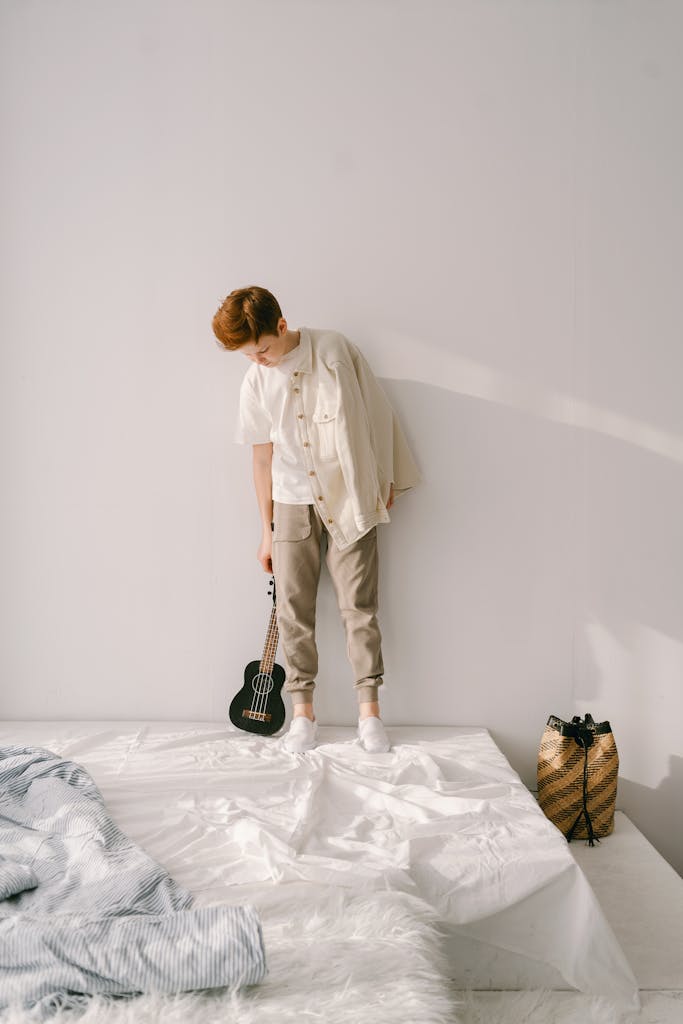 A young man stands indoors with a ukulele, embodying a relaxed and minimalist lifestyle.