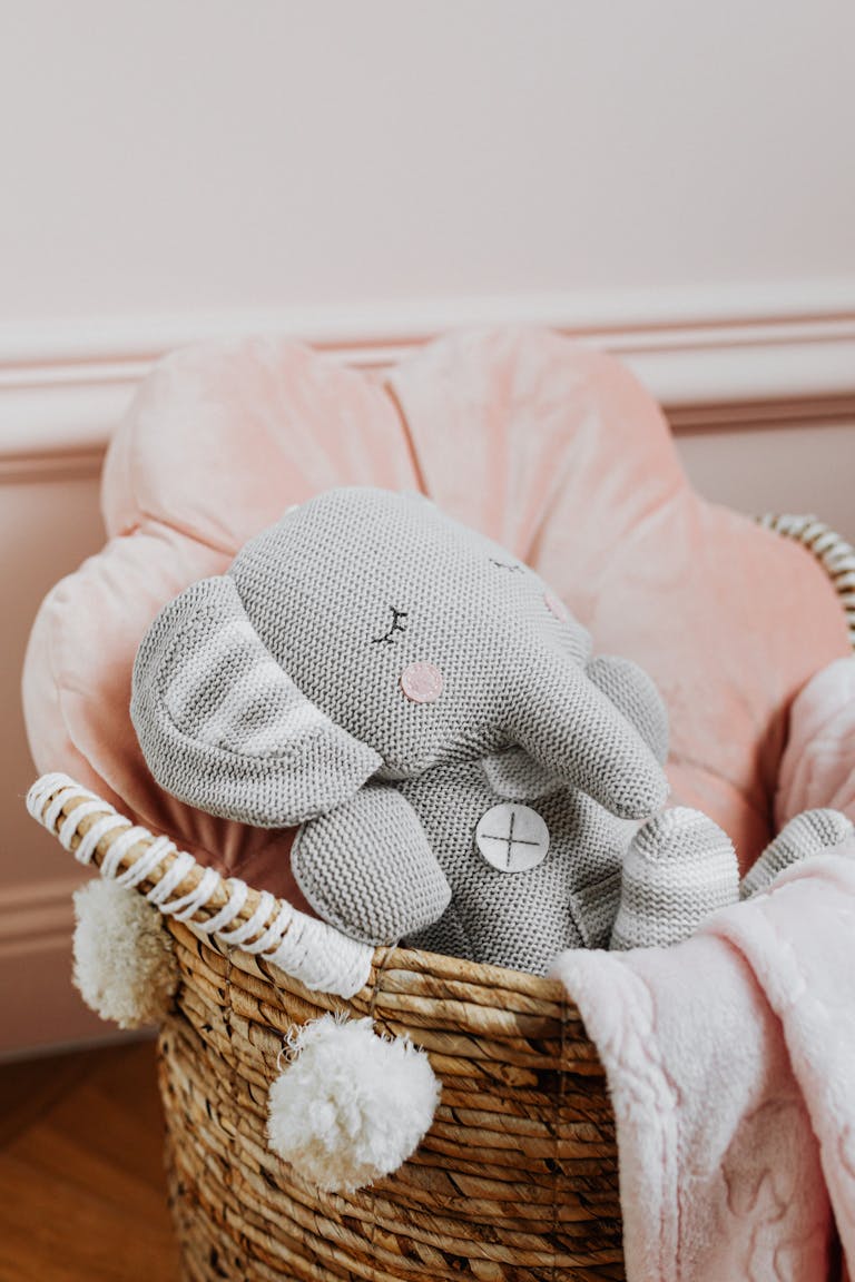 Adorable stuffed elephant toy nestled in a soft woven basket with pink lining.