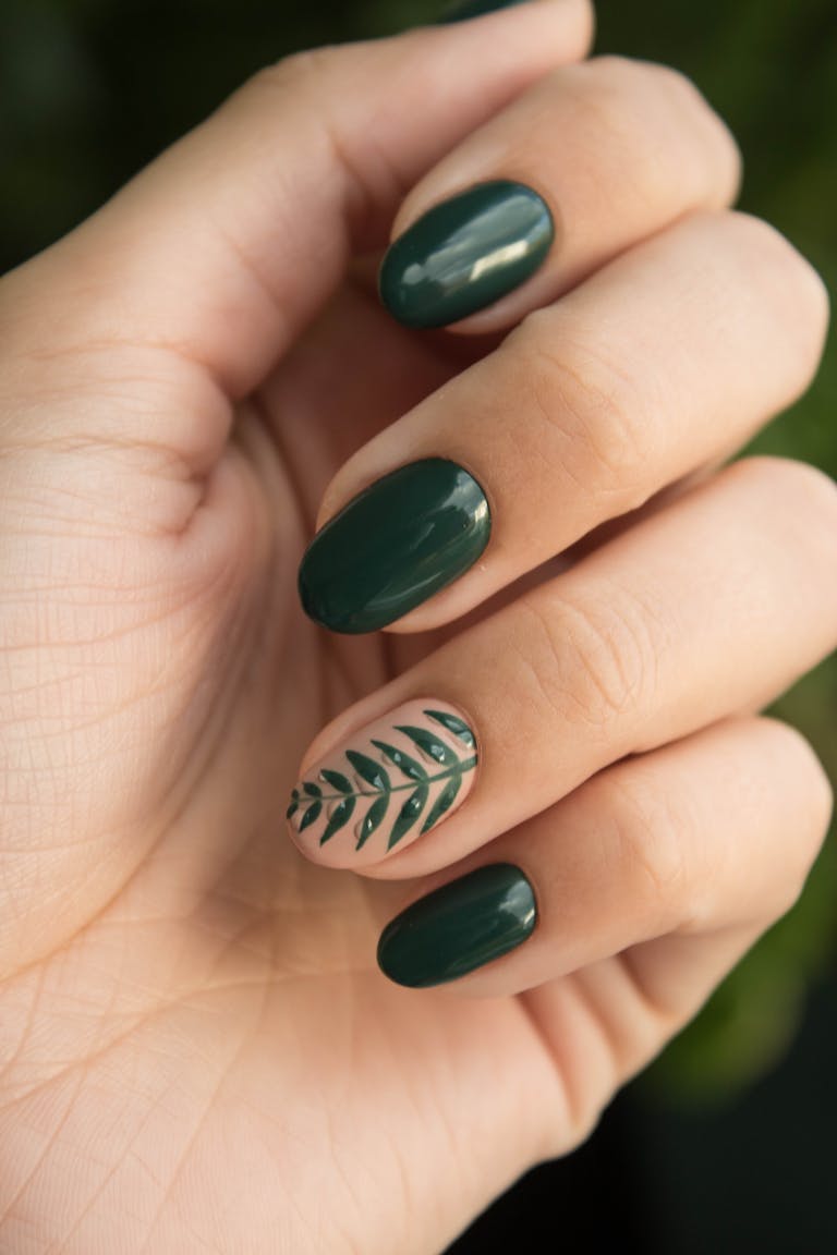 Close-up of a stylish green manicure with a leaf design, showcasing glossy fingernails and natural skin tone.