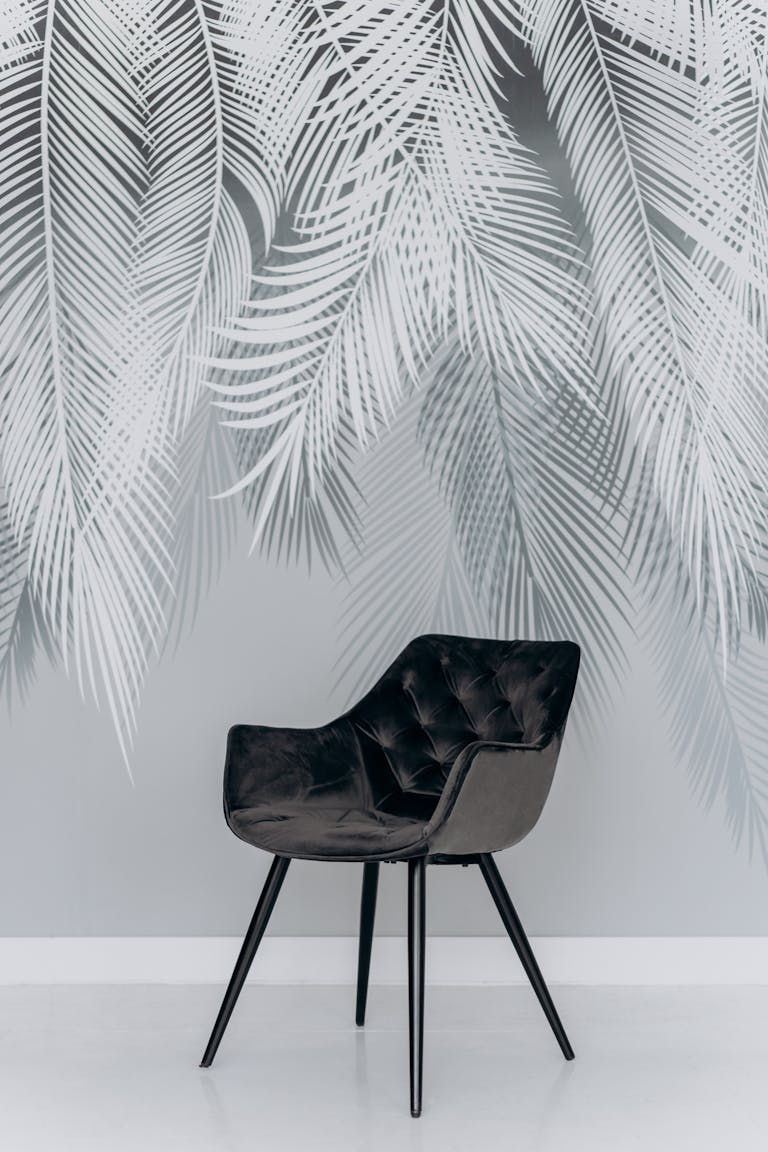 Stylish black chair featured against a grey palm leaf patterned wall, exuding contemporary elegance.