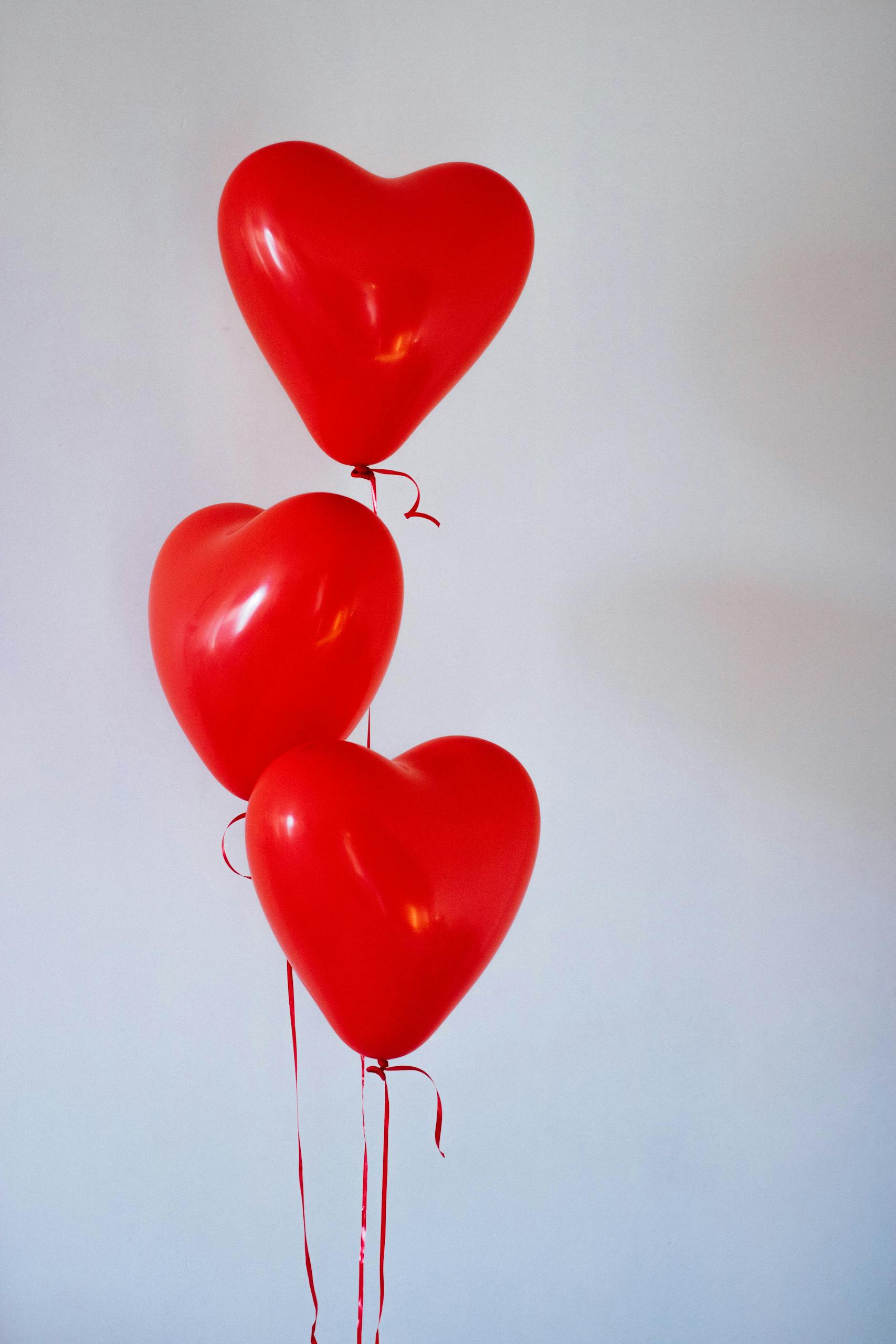 Three red heart-shaped balloons floating in a minimalist studio setting, evoking love and romance.