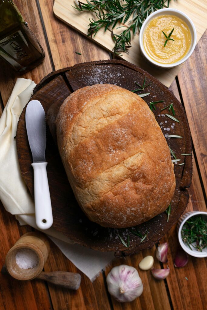 Freshly baked artisan bread on a wooden board with rosemary and garlic, perfect for gourmet meals.